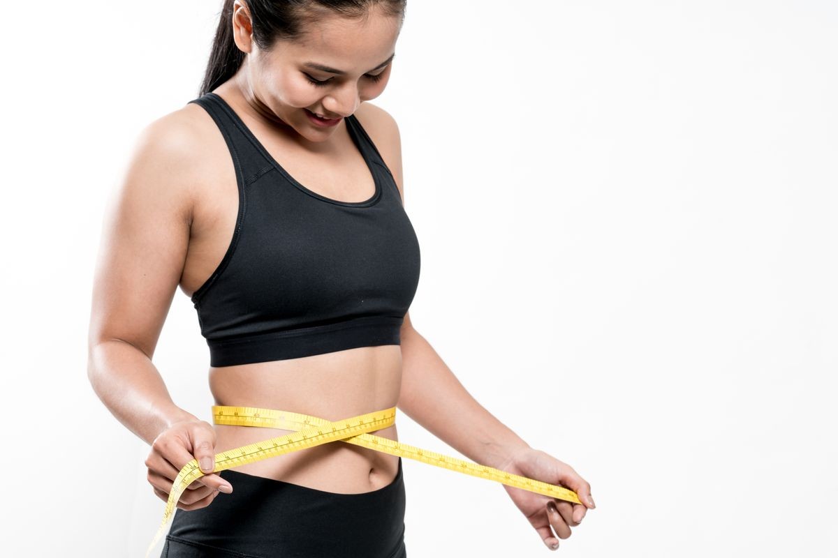 Slim young woman measuring her waist with a measure tape. Weight loss concept.