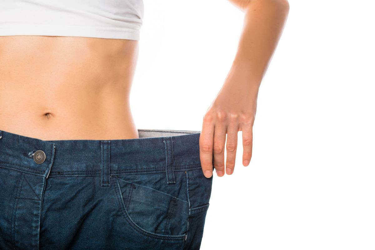 Slim stomach of young woman, thin body with perfect waist, showing her jeans after successful diet or sport training on isolated background. Weight loss and slimming