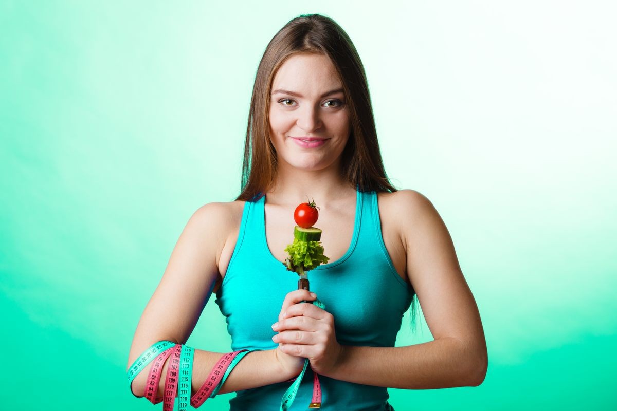 Weight loss and dieting concept. Sporty girl fitness woman holding fork with vegetarian food on green blue background in studio.